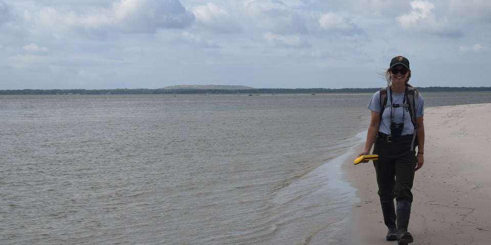 A woman walks at the edge of the water with a small GPS unit. A woman walks at the edge of the water with a small GPS unit.
