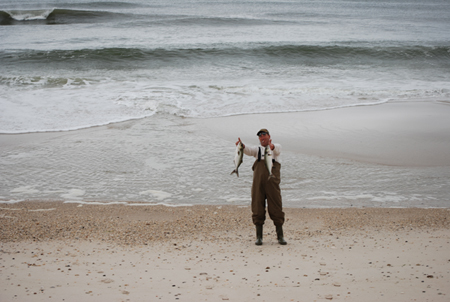 Fisherman with bluefish in surf.