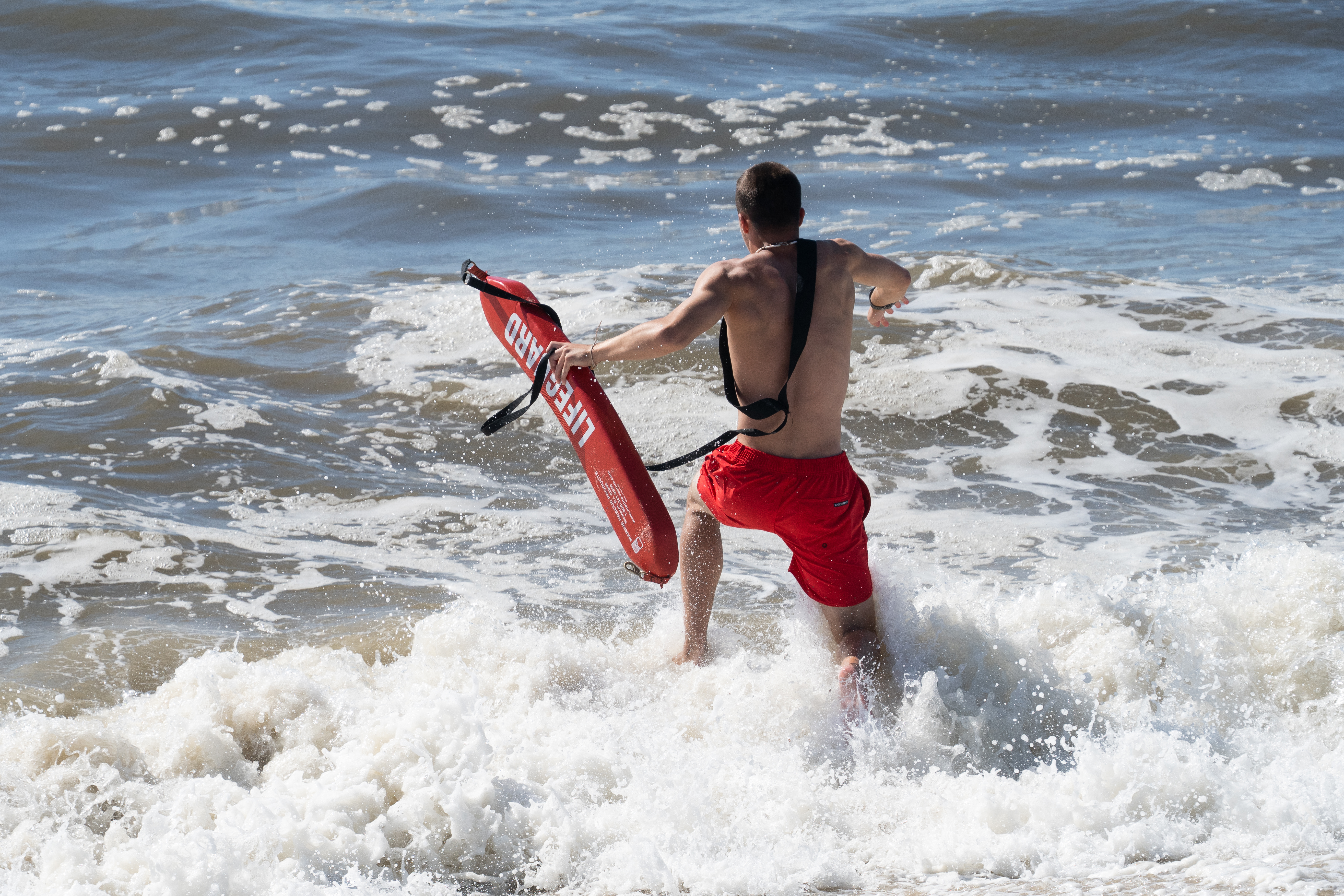 Lifeguard in Surf A lifeguard runs into the surf with float.