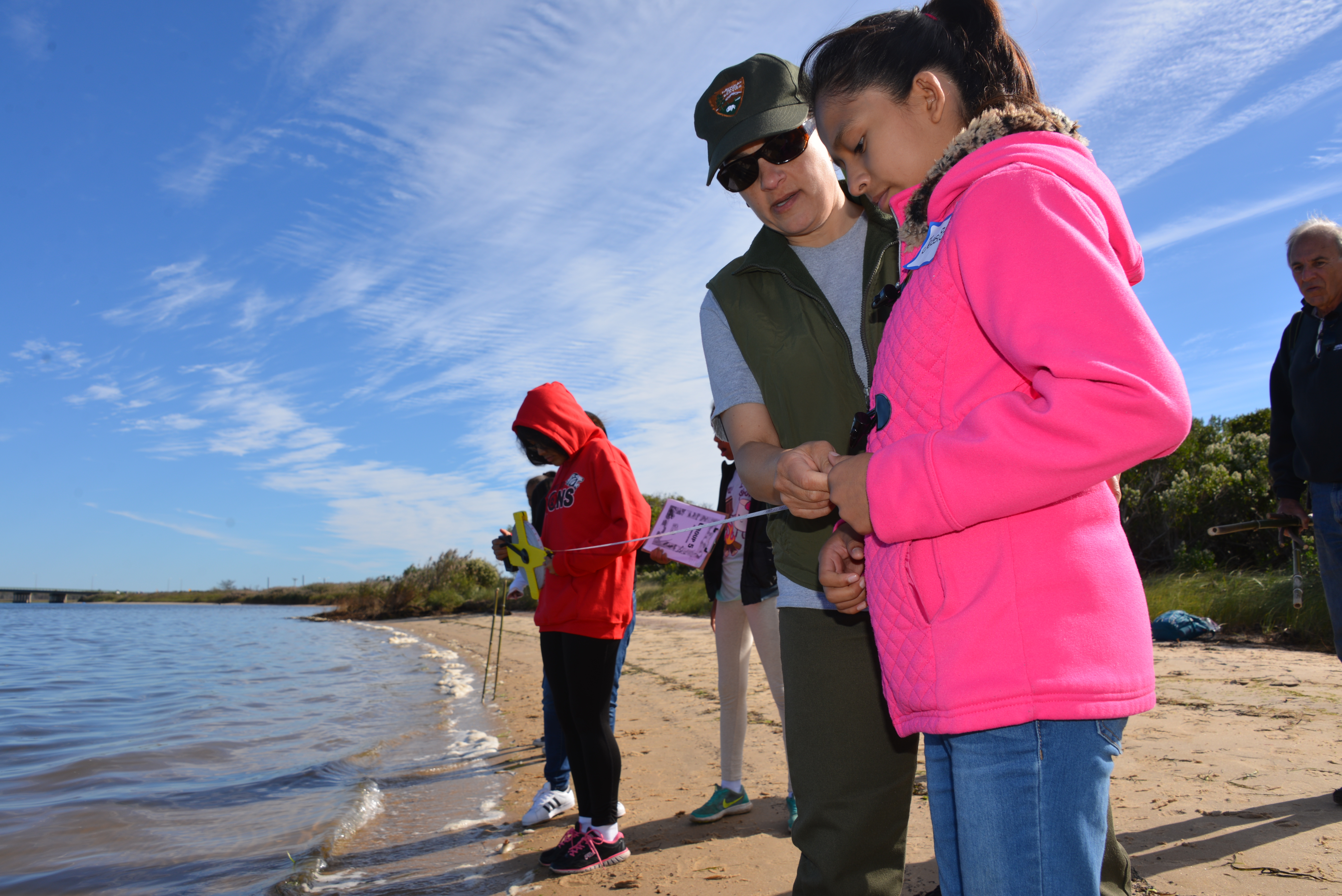 Students use a measuring tape along the shoreline with a park ranger.