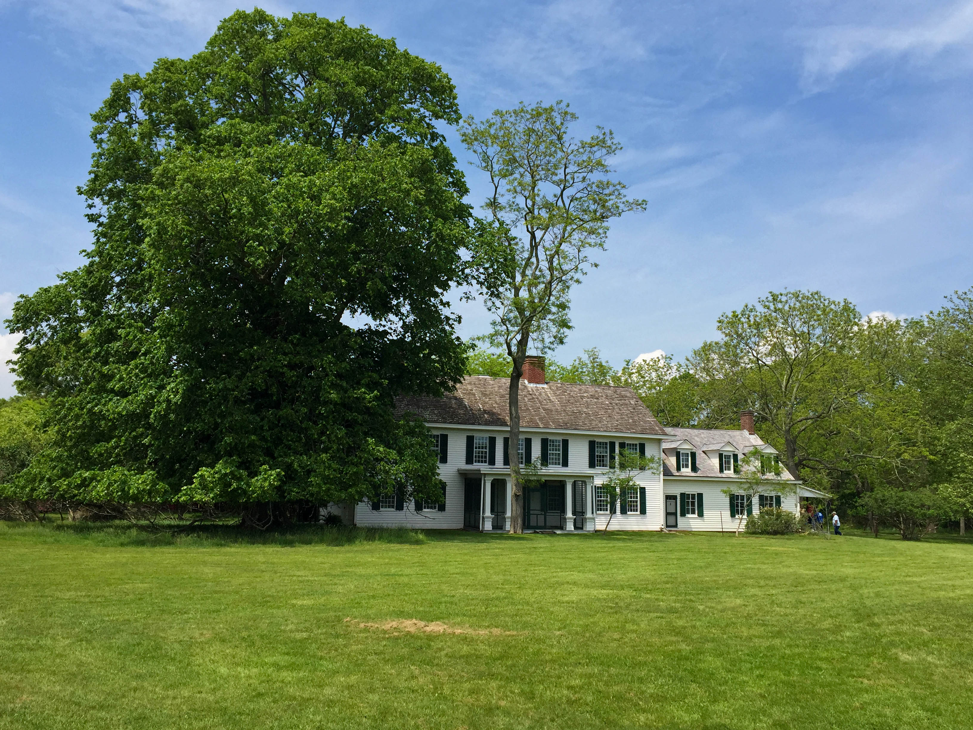 View of large, white historic home from lush green field.