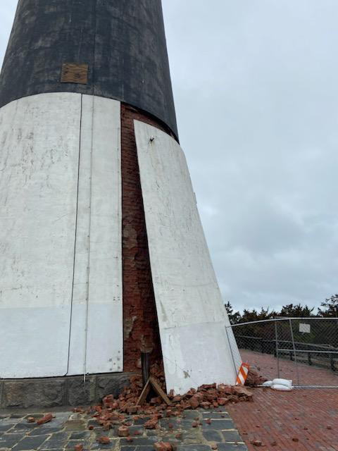 Fire Island Lighthouse Damage. Photo of a white lighthouse panel propped against brick with fallen bricks around the base of the building