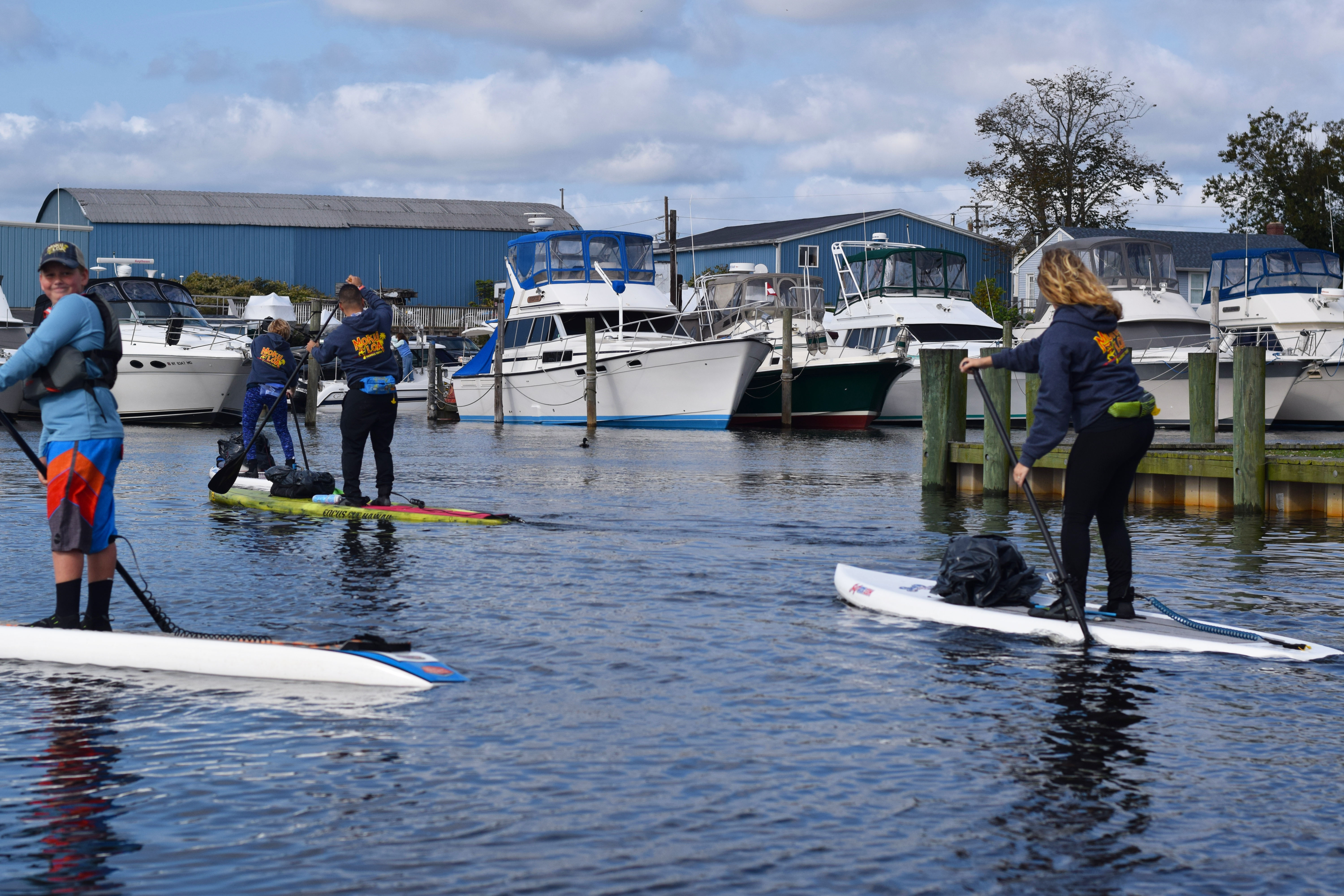 Stand up paddle boarders paddle on the Patchogue River with garbage bags on board for a volunteer cleanup.
