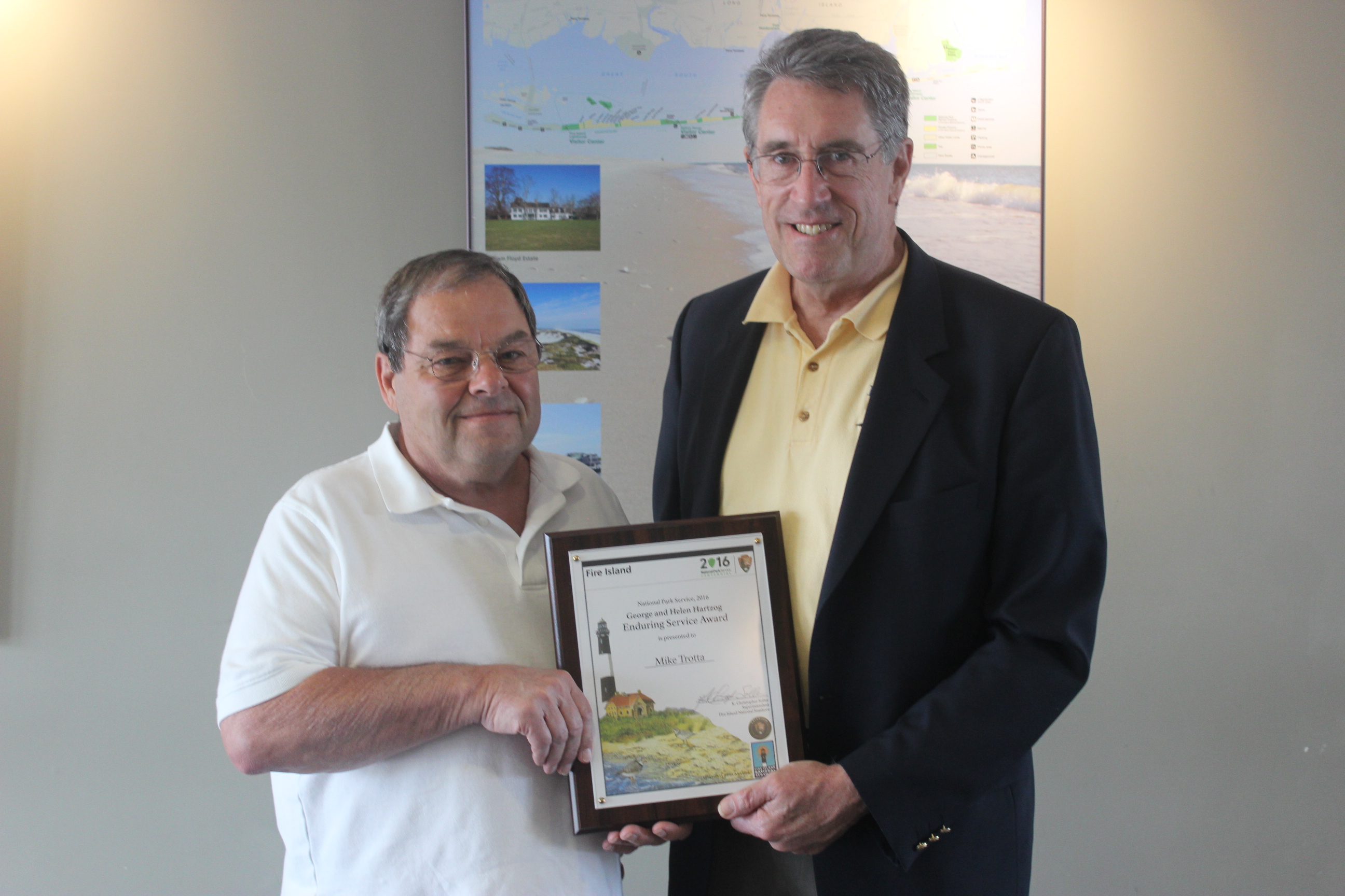 Two men shake hands and hold award certificate.