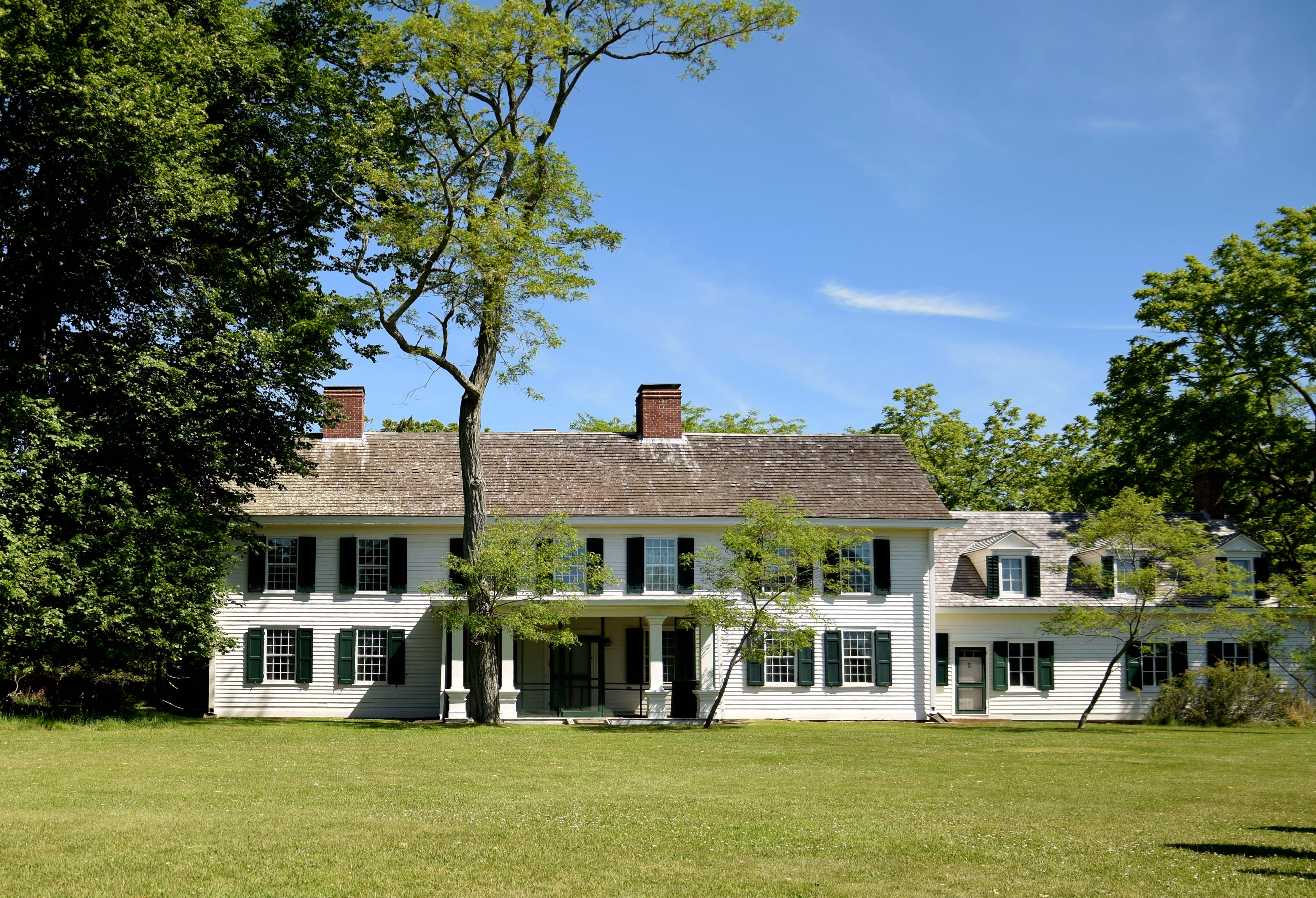 A large white historic home surrounded by lush green lawn and trees