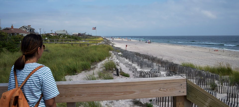 Visitor overlooks dunes, beach, and ocean from boardwalk.