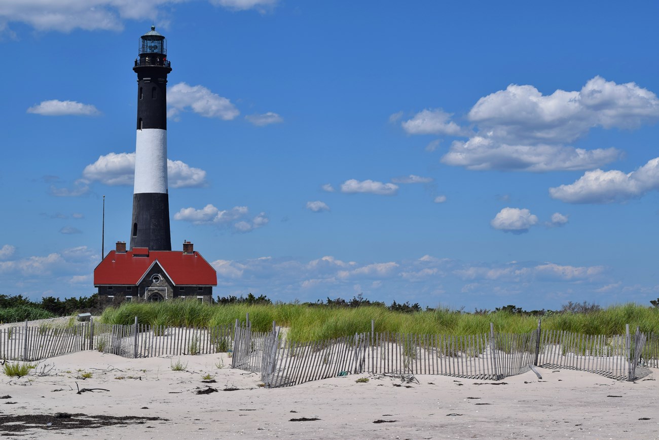 Black and white lighthouse tower and nearby buildings stand out against a sunny blue sky.