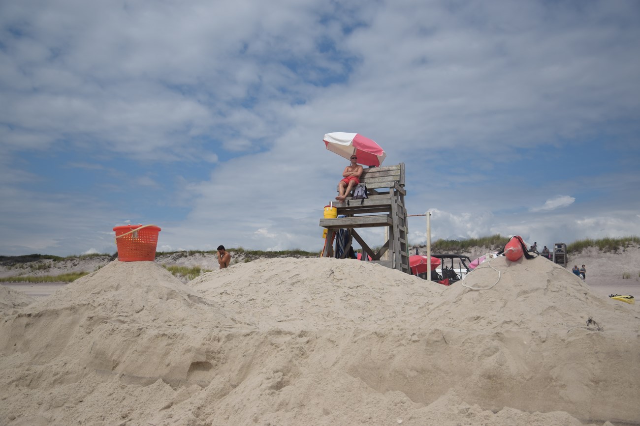 A lifeguard sits in a lifeguard chair on a sandy beach.