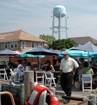 Man walks toward dockside boat, leaving colorful umbrellas over restaurant's small tables.