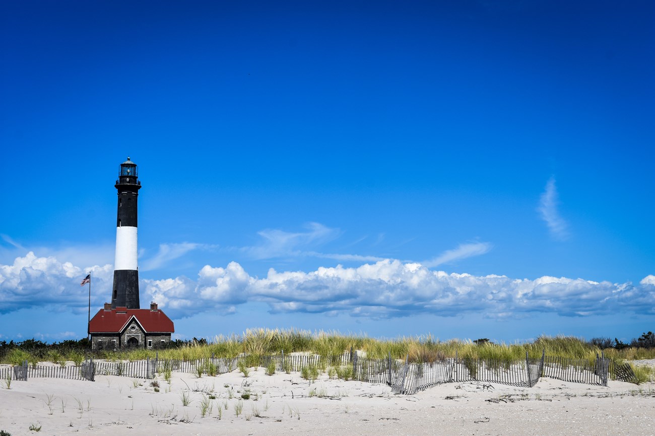 View from beach of black and white lighthouse tower and keepers quarters with red roof.