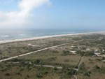 Aerial view of boardwalks meandering from a large parking lot, ocean waves in the background.