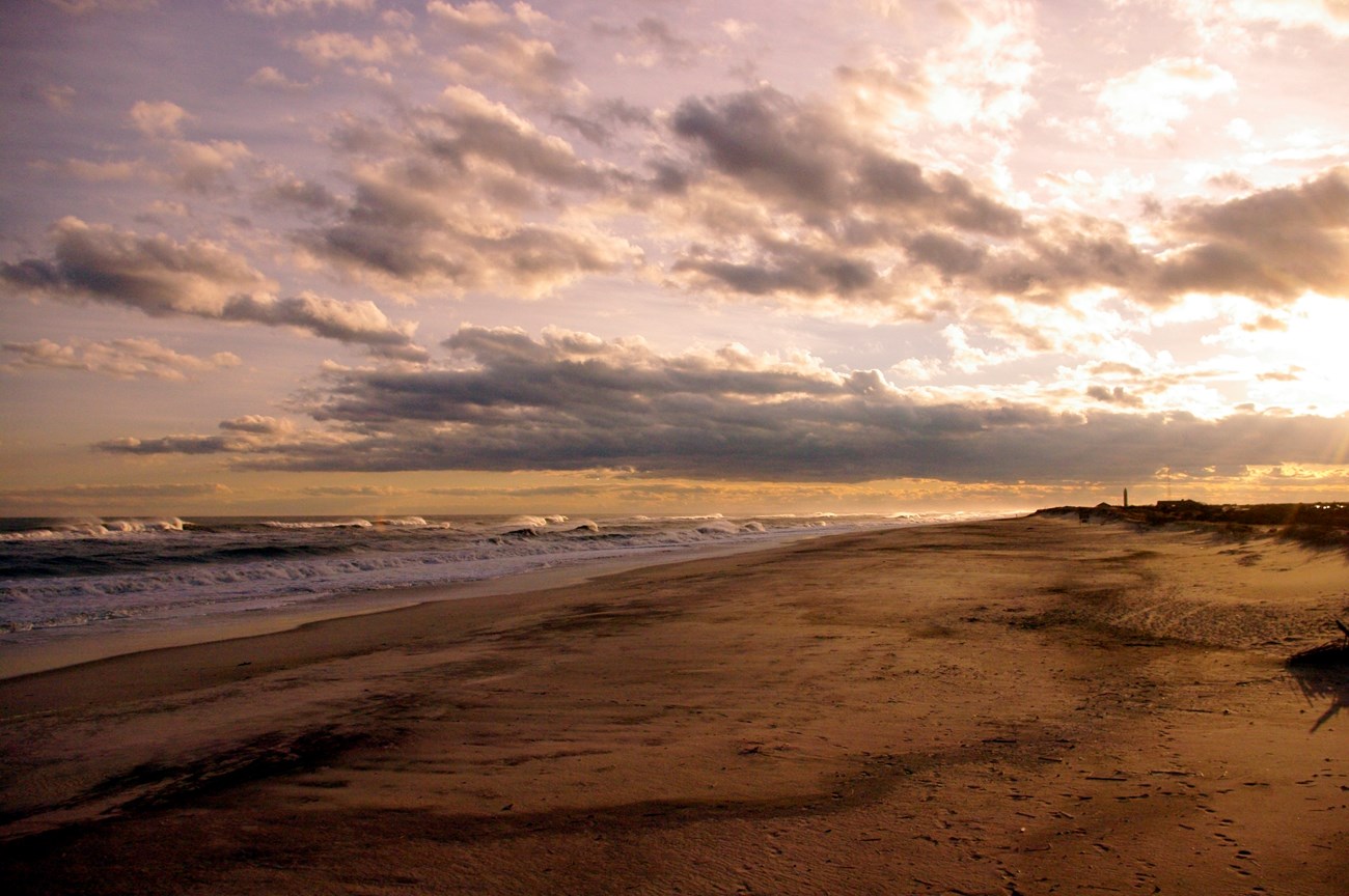 Clouds lit by the setting sun float over the beach and waves.