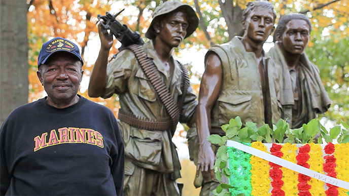 U.S. veteran stands in front of statue of three men in military uniform U.S. veteran stands in front of statue of three men in military uniform
