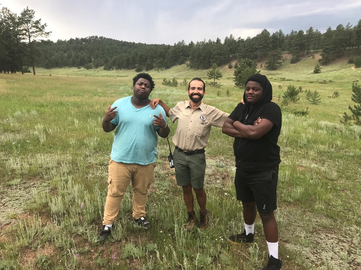 Education Intern, Kevin Jauregui stands next to hip hop artists Nehemiah Vaughn and Joey Lovett in a grassy meadow at Florissant Fossil Beds.