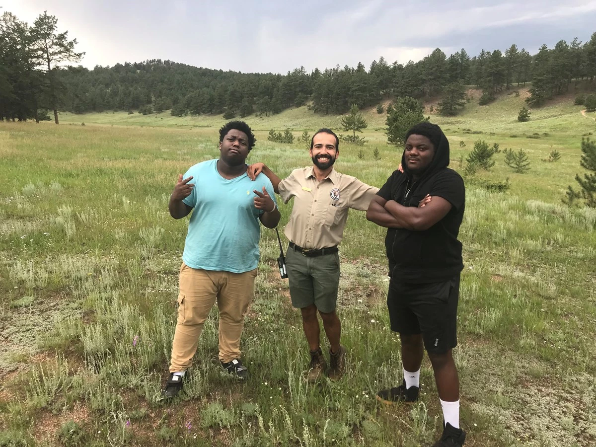 FIGURE-1-FLFO-ARTICLE-PARK-PALEO-NEWSLETTER Education Intern, Kevin Jauregui stands next to hip hop artists Nehemiah Vaughn and Joey Lovett in a grassy meadow at Florissant Fossil Beds.