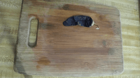 Moving image showing six dried chile peppers placed one by one on a wooden cutting board. A small knife is used to remove the seeds from each one. Then each seeded dried chile pepper is removed from the cutting board.
