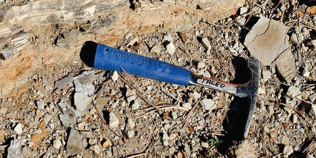 a blue handled rockhammer amongst broken shale