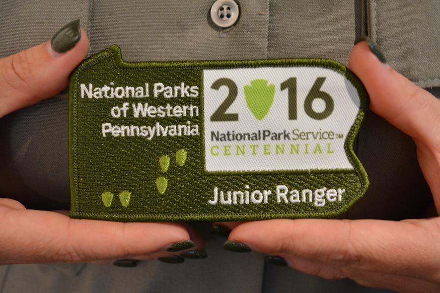 Patch in the shape of Pennsylvania.  Green with white lettering and small lighter green arrowhead shapes.  Writing:  National Parks of Western Pennsylvania Junior Ranger.