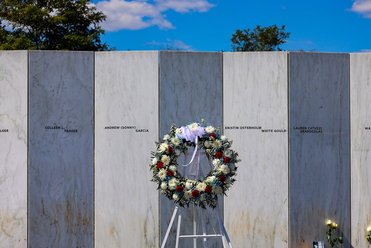 A wreath placed in front of a white marble wall with names inscribed into it.