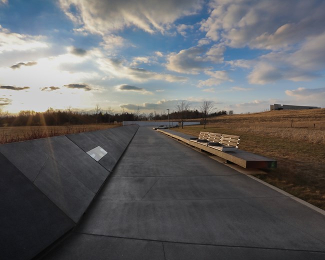 Black sloping wall leads to a white marble wall in the distance with a blue sky overhead and sunset beyond the walls.