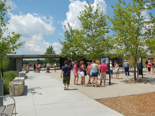 Visitors standing outside under trees reading signs in front of a grey rectangular shaped shelter.