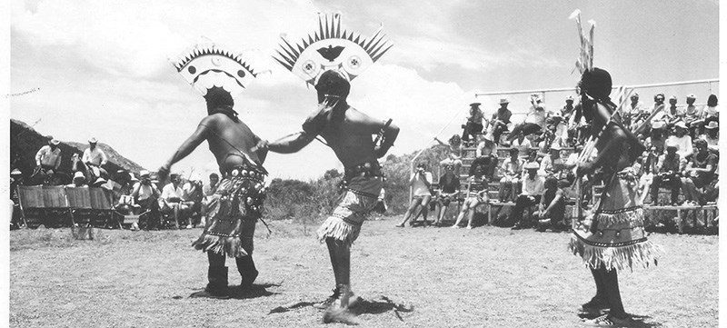 Black and white photo of Apache Dancers wearing traditional masks and headresses