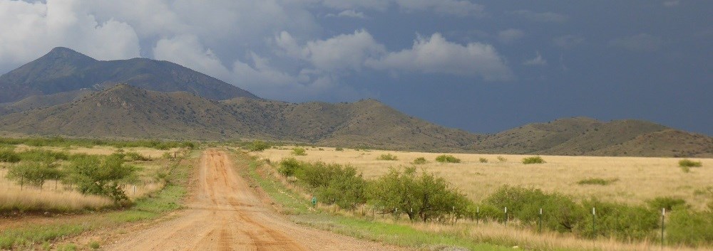 A dirt road stretches into the mountains under stormy skies