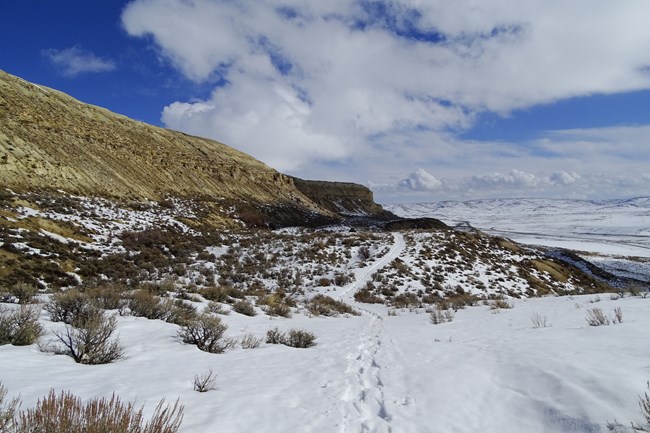 Footsteps lead a path through the snow with a rocky ridge on the left along the Historic Quarry Trail.