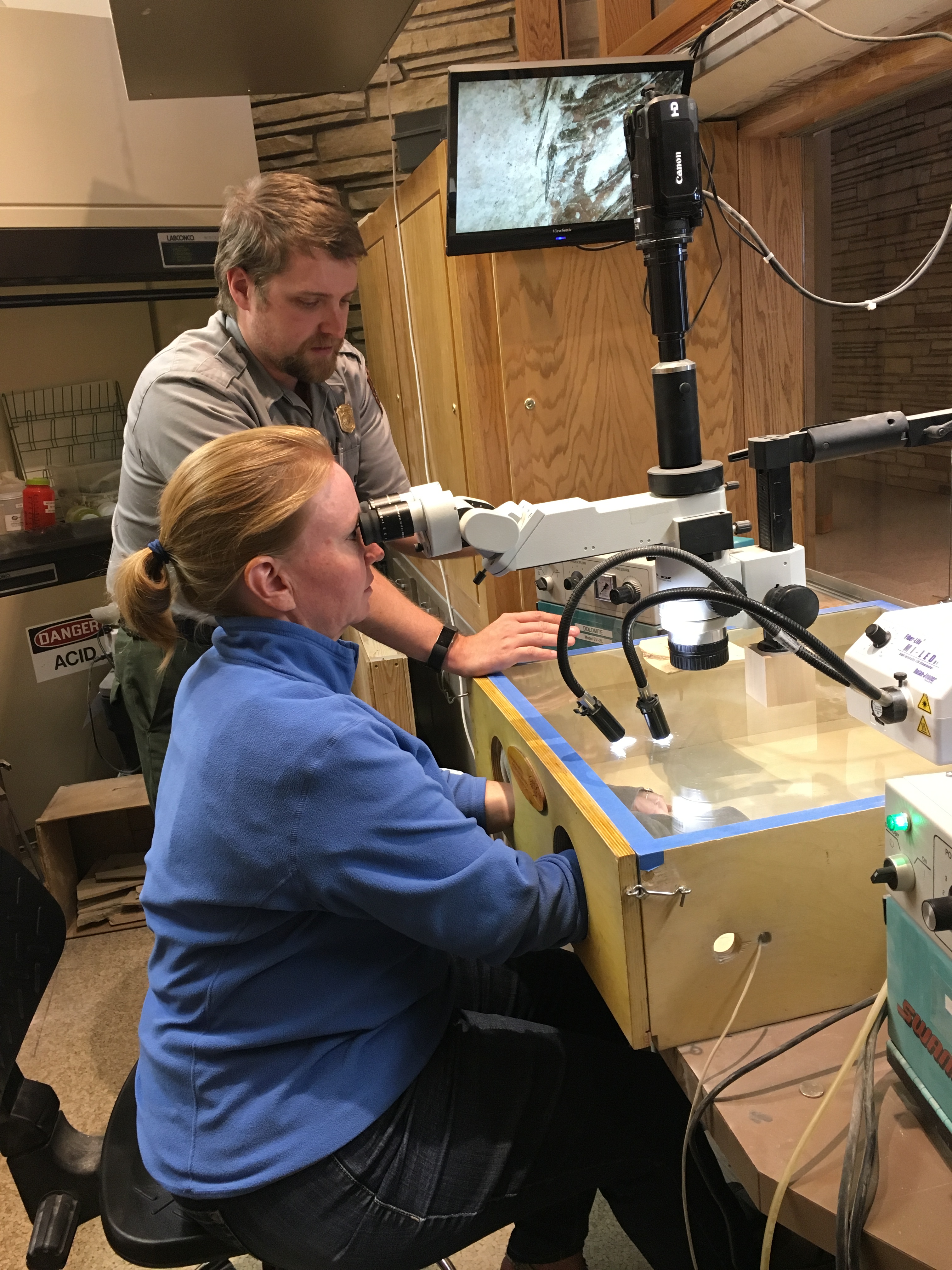 A ranger watches while a visitor looks through a microscope