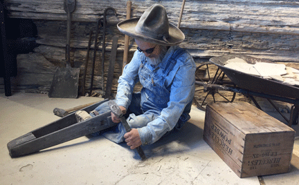 A mannequin with a peg leg uses a hammer and chisel on rock.