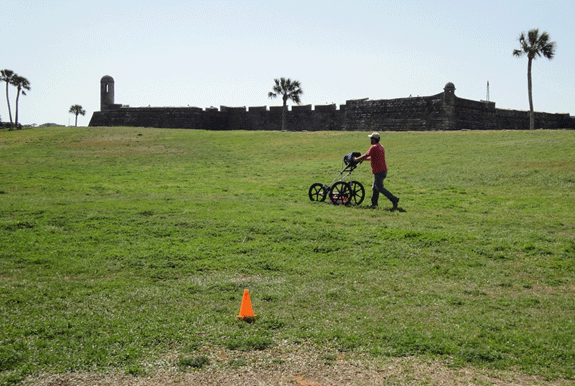 person pushing ground pentrating radar equipment across green grass