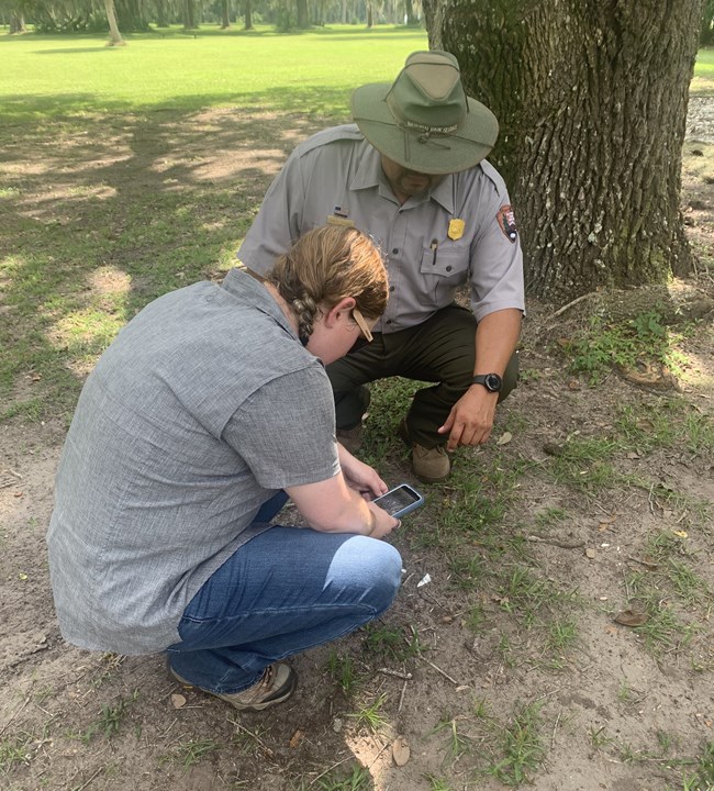 A park ranger watches as a visitor photographs an artifact on the ground