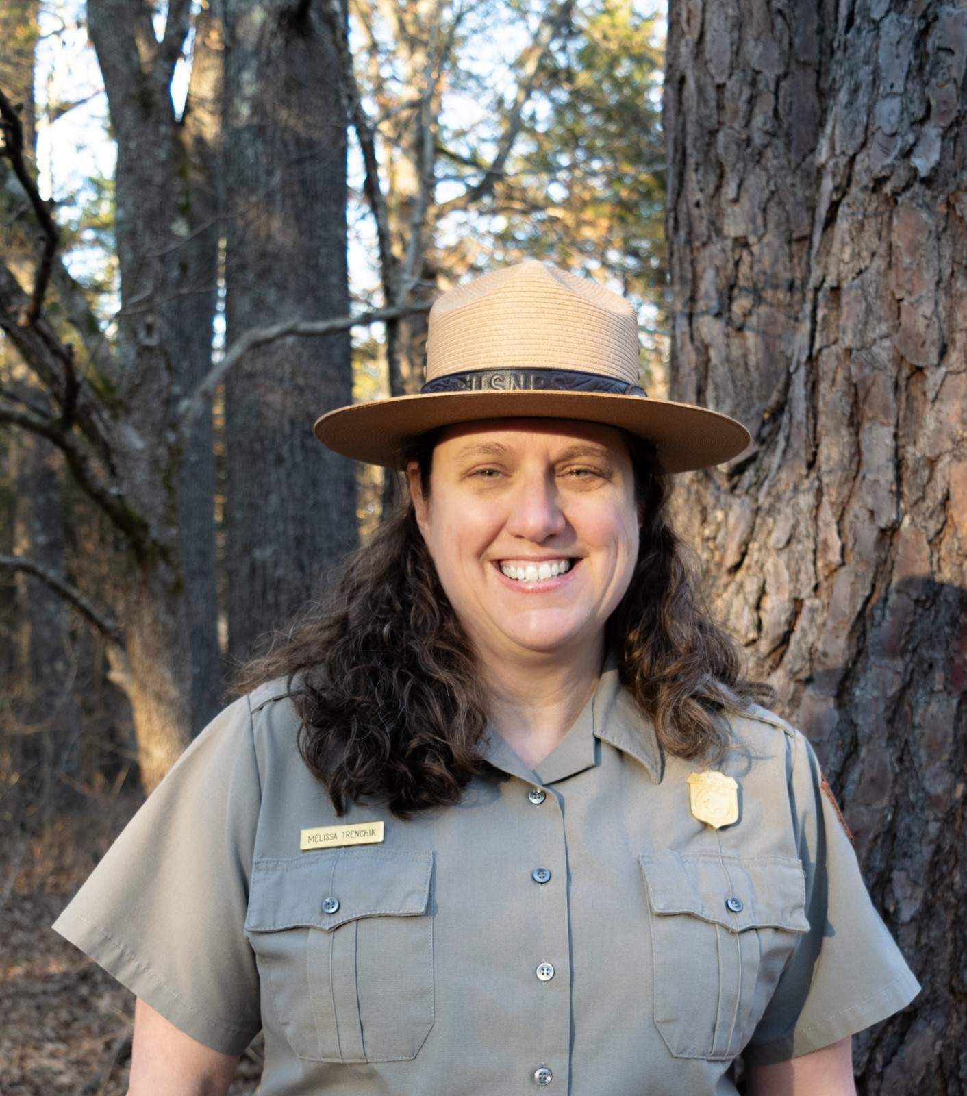 Melissa Trenchik, superintendent, dressed in flat hat, grey uniform shirt standing in front of a few trees.