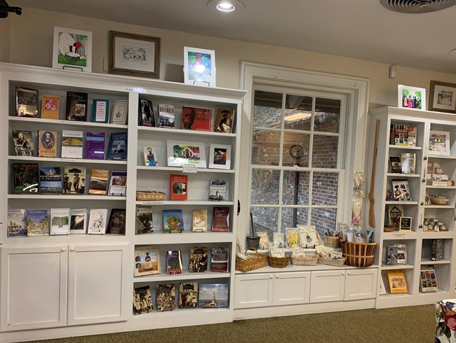 Floor to ceiling colonial style white bookshelves displaying books, games, and art associated with Fort Frederica history.