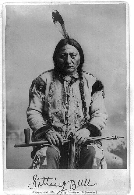 Historical image of a Native American man with a gun, dressed in traditional clothing,