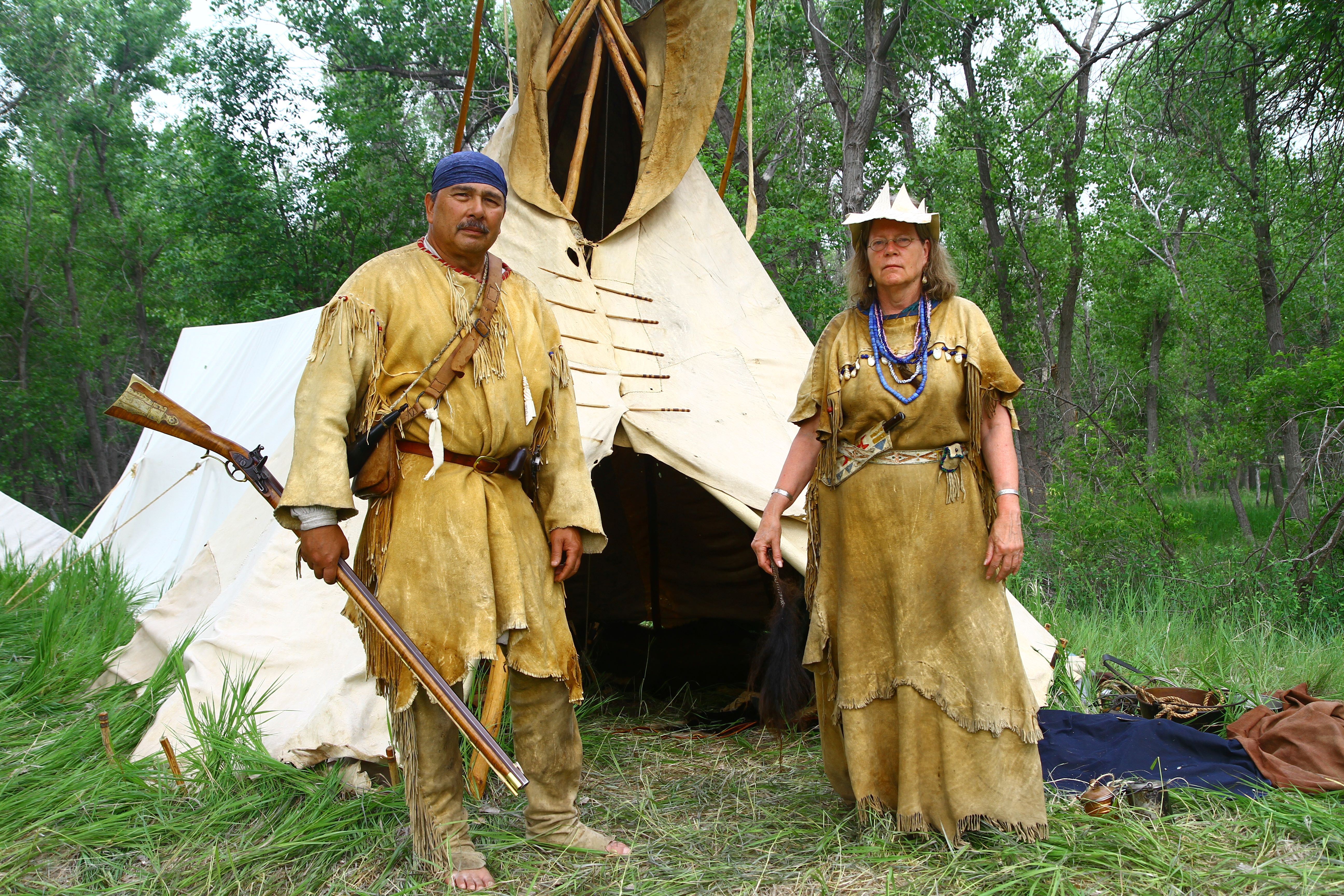 Two individuals in traditional attire stand beside a teepee, showcasing cultural heritage and connection to nature
