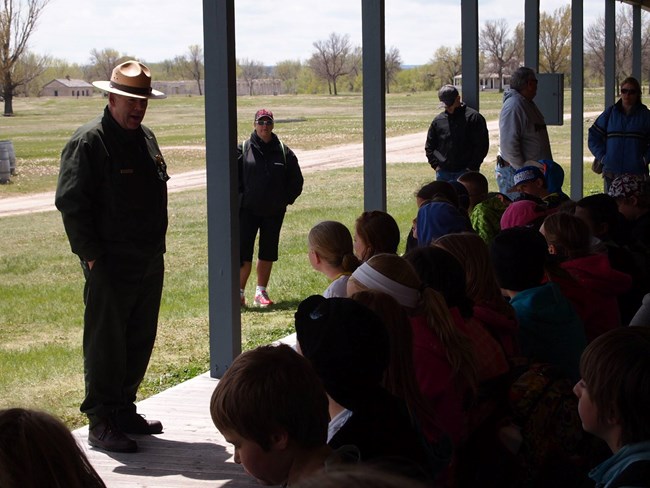 A Ranger talking to kids sitting on a long porch.