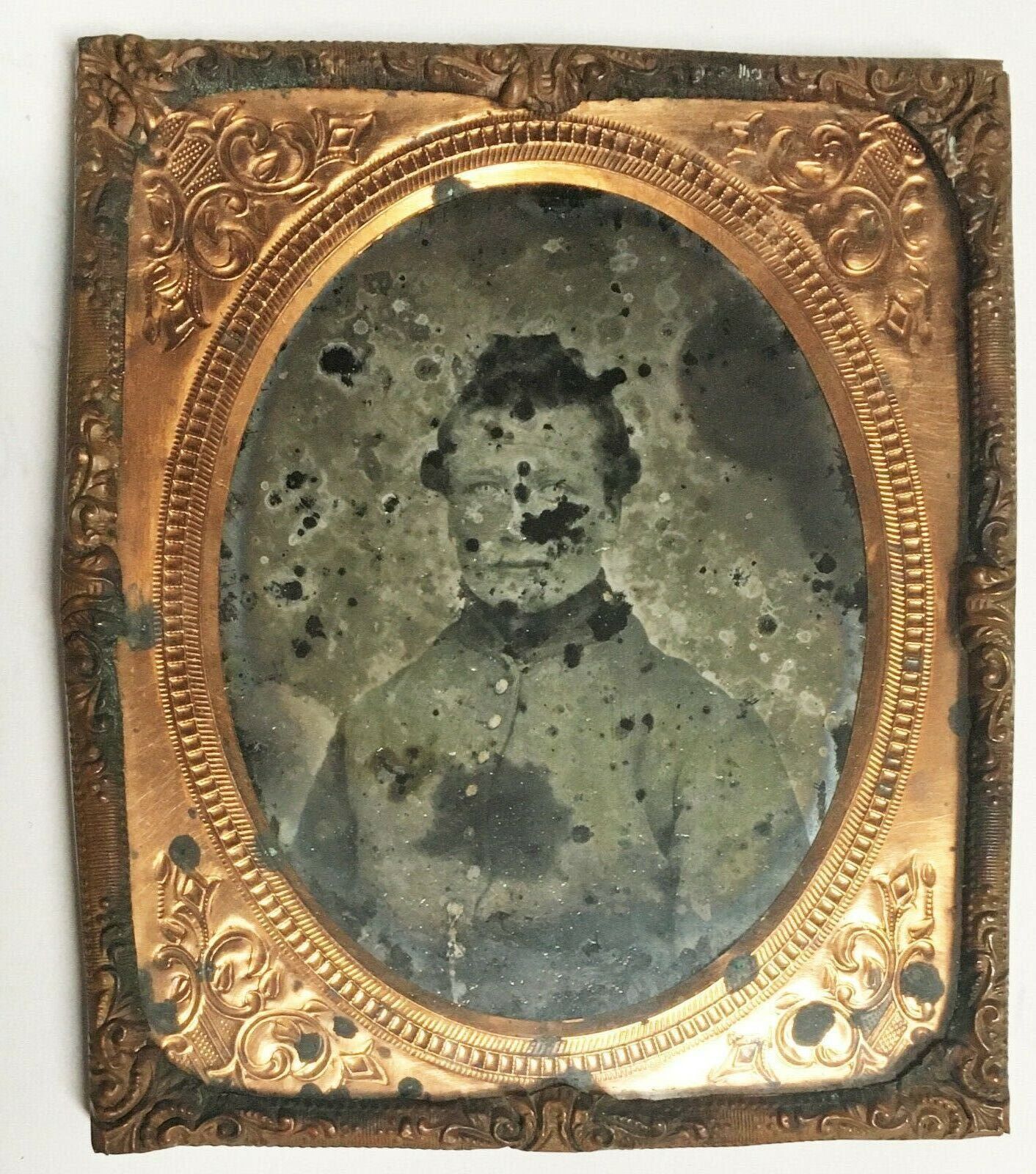 A damaged black and white photograph of a man in an artillery shell jacket. Around the photo is a brass and gold stamped frame.