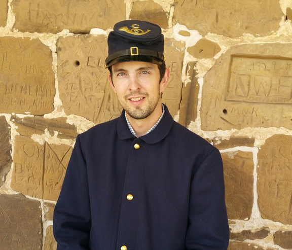 Young man sitting on bench wearing 19th century U.S. Army uniform.