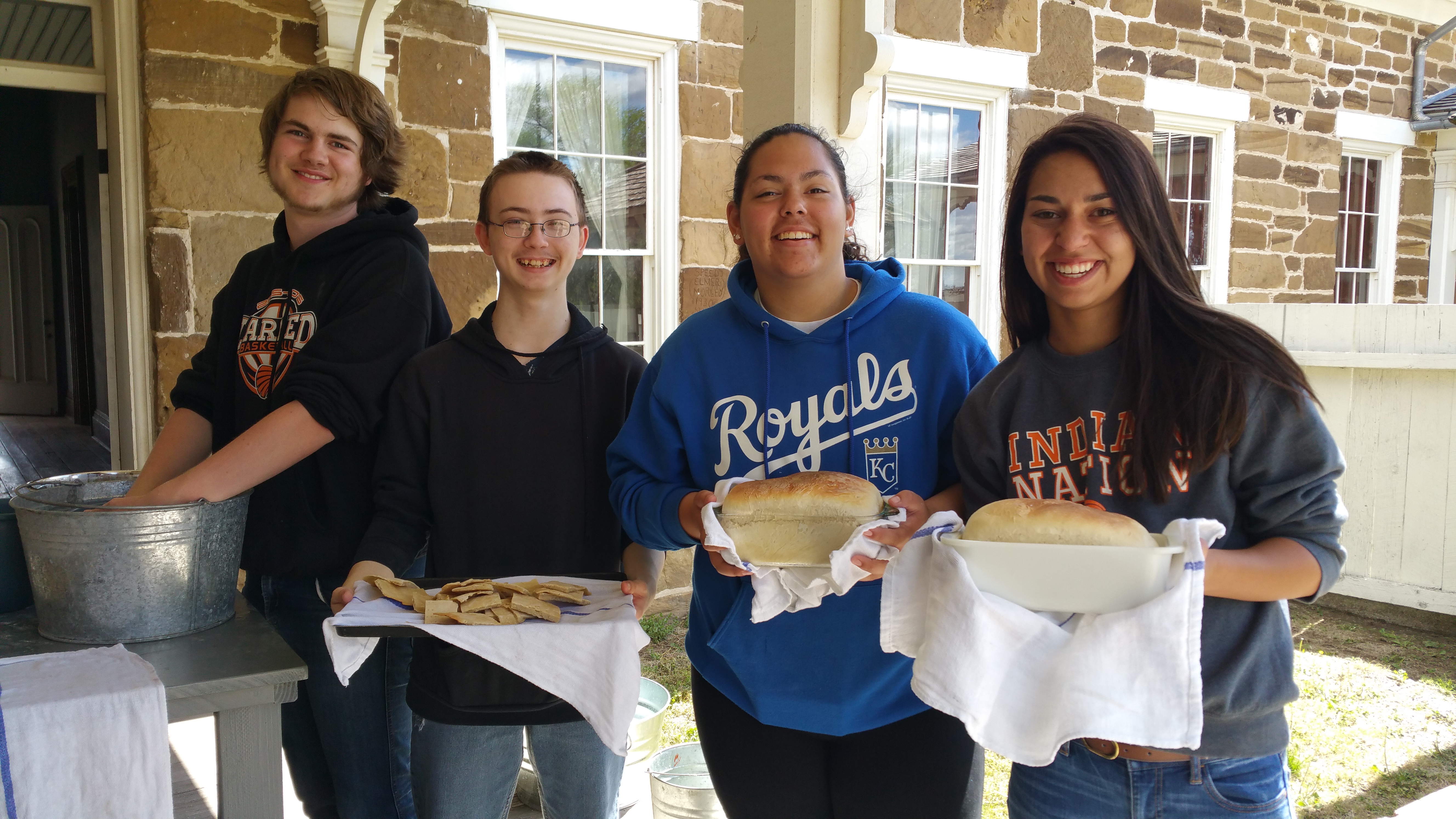 Teens holding freshly baked bread in bread pans.