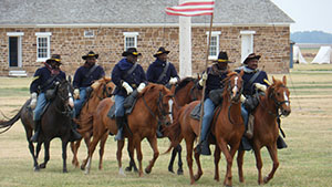 African American men in 19th century US Army uniforms on horseback.