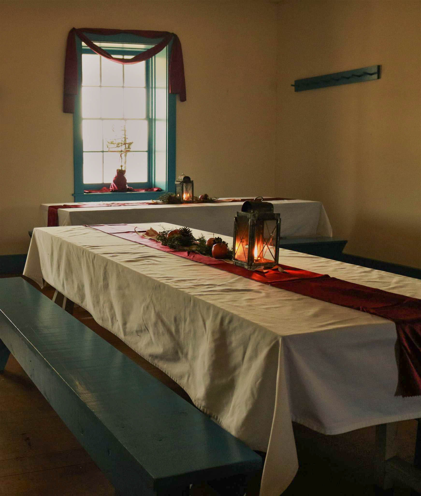 a color photograph of a room decorated for Christmas with runners, tablecloths, pinecones, lanterns, and greenery.