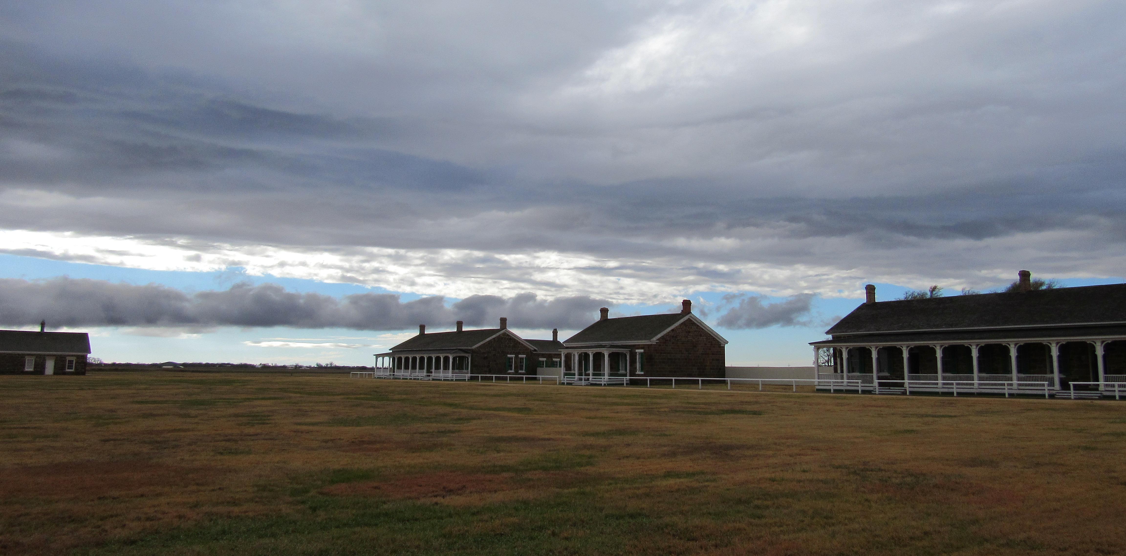 Three sandstone buildings viewed across a grassy field.