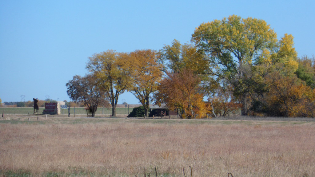 Changing Color at Fort Larned Highway Rest Area Broadleaf trees are in fall colors around a picnic area and restroom next to a two-lane rural highway.