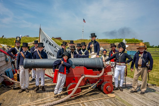 Living historian sailors pose with naval cannon with fort in background