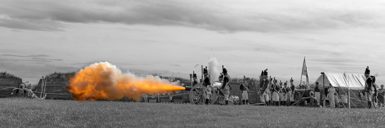 War of 1812 artillery demonstration. Crew beside six-pound field gun with fireball from muzzle