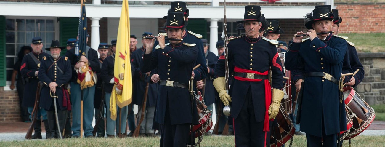 A group of musicians in Civil War uniforms in the star fort with a group of Civil War living historians in the background.