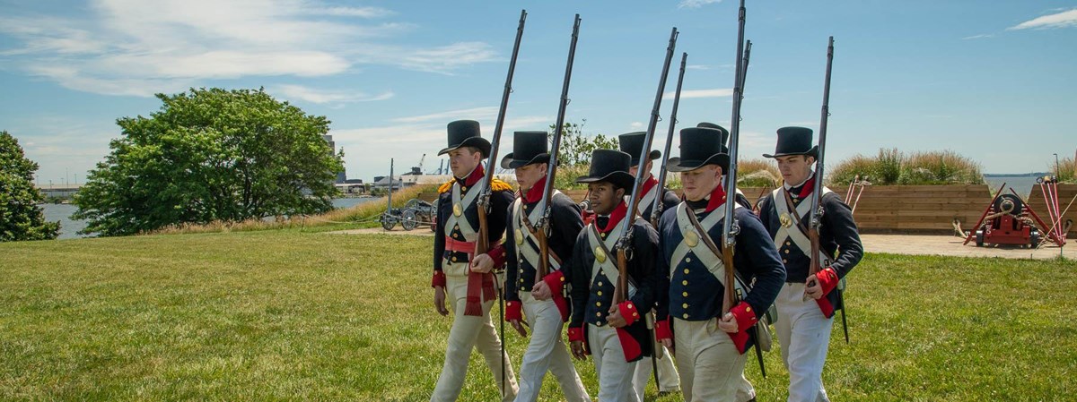 a modern day photograph of living historians dressed in militia gear with muskets marching together.