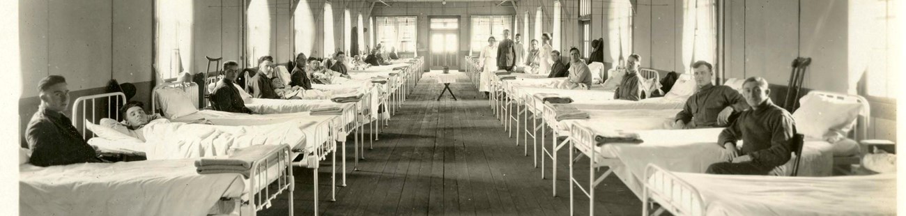 A black and white photograph of rows of hospital beds with patients in them looking towards the camera.