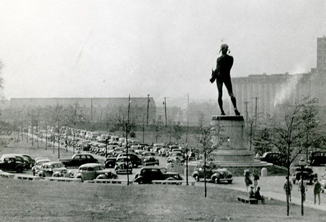 A black and white photograph of a monument with cars parked around it.